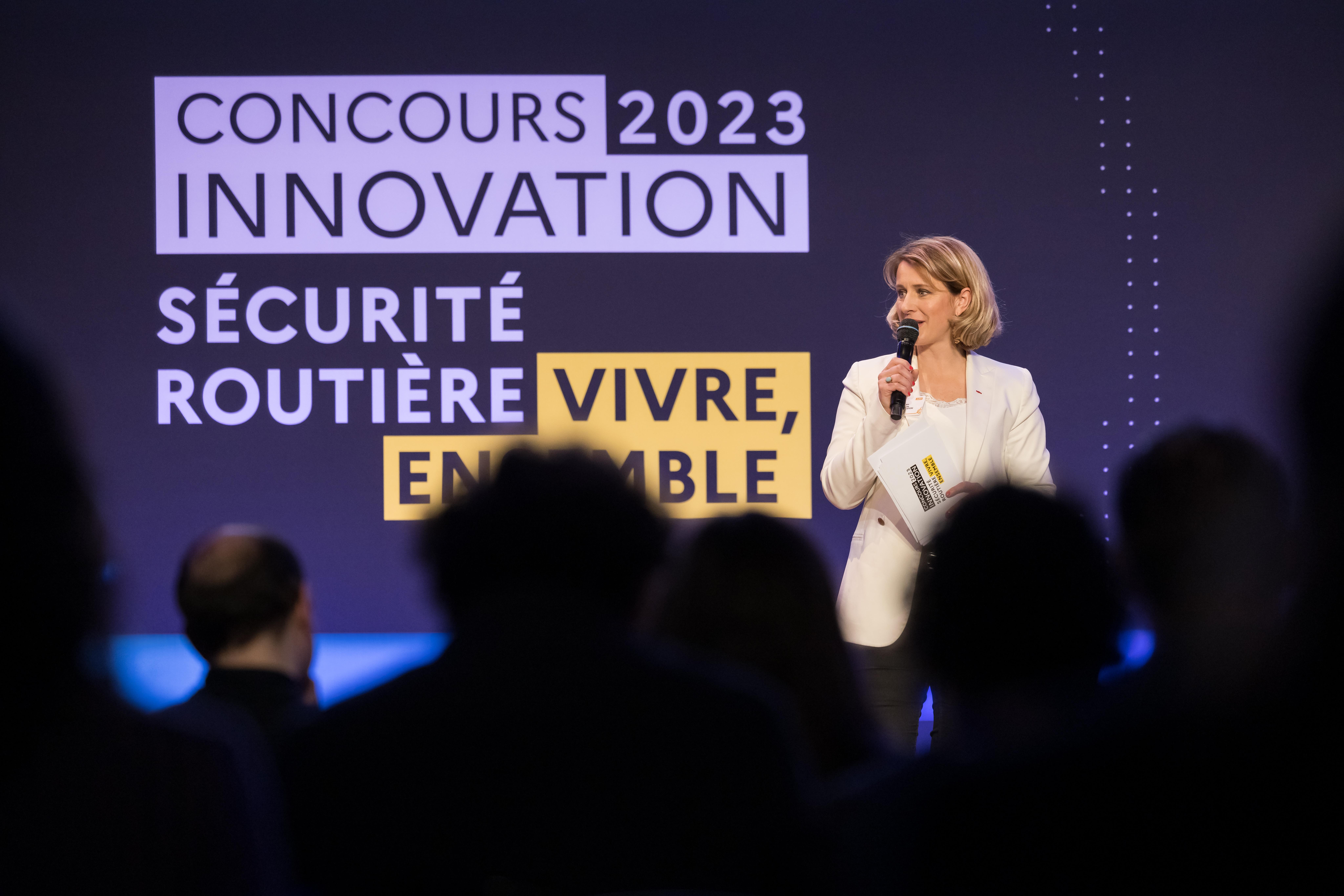 Photographie de la cérémonie de remise des lauréats 2023 présentant une femme parlant, micro à la main devant le logo du prix innovation 2023 projeté sur un grand écran, derrière en fond.